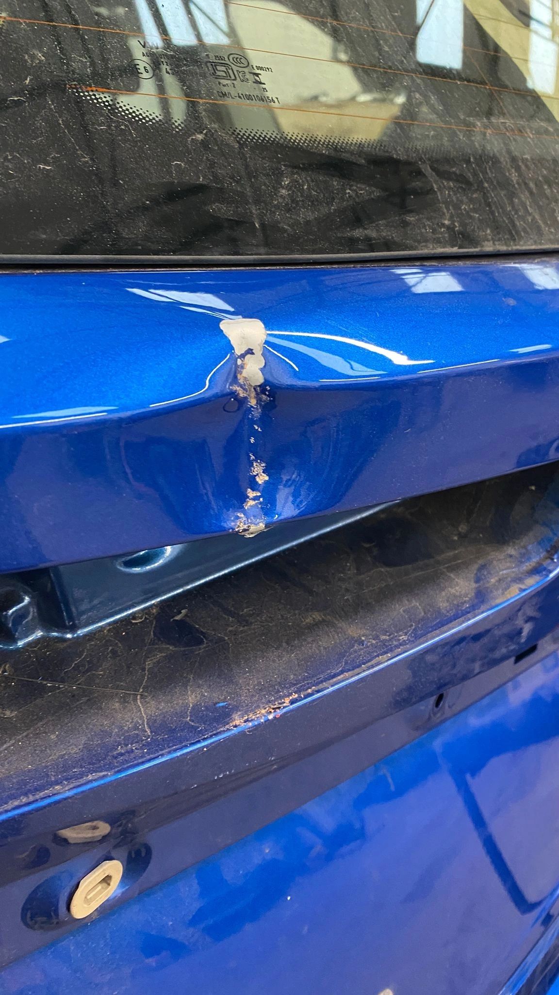 Close-up of a chipped blue car panel showing the paint layers under the colour coat