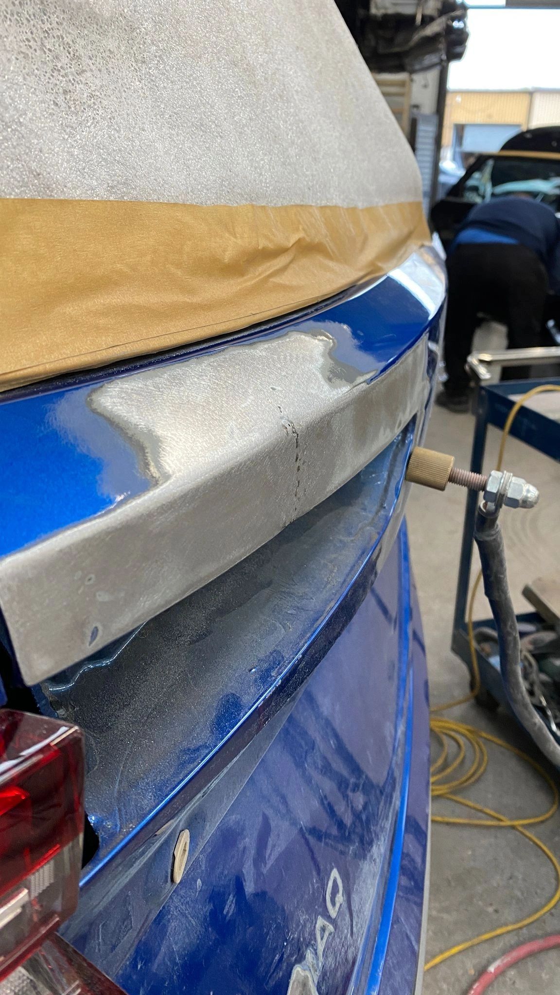 Body filler being spread and shaped over a dent on a blue car panel during a repair