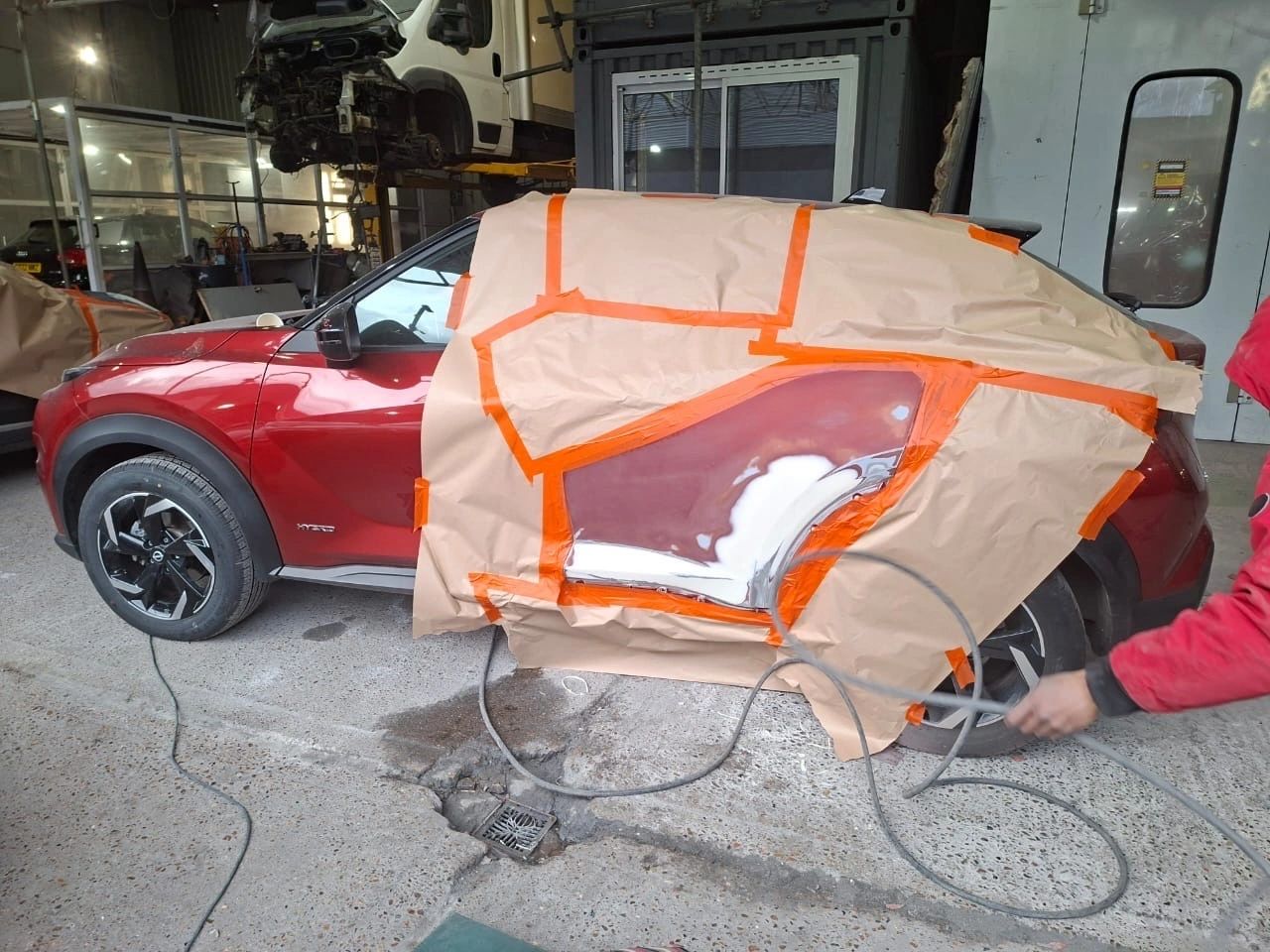 A red Citroen being resprayed under spray booth lighting with fresh paint on the panels