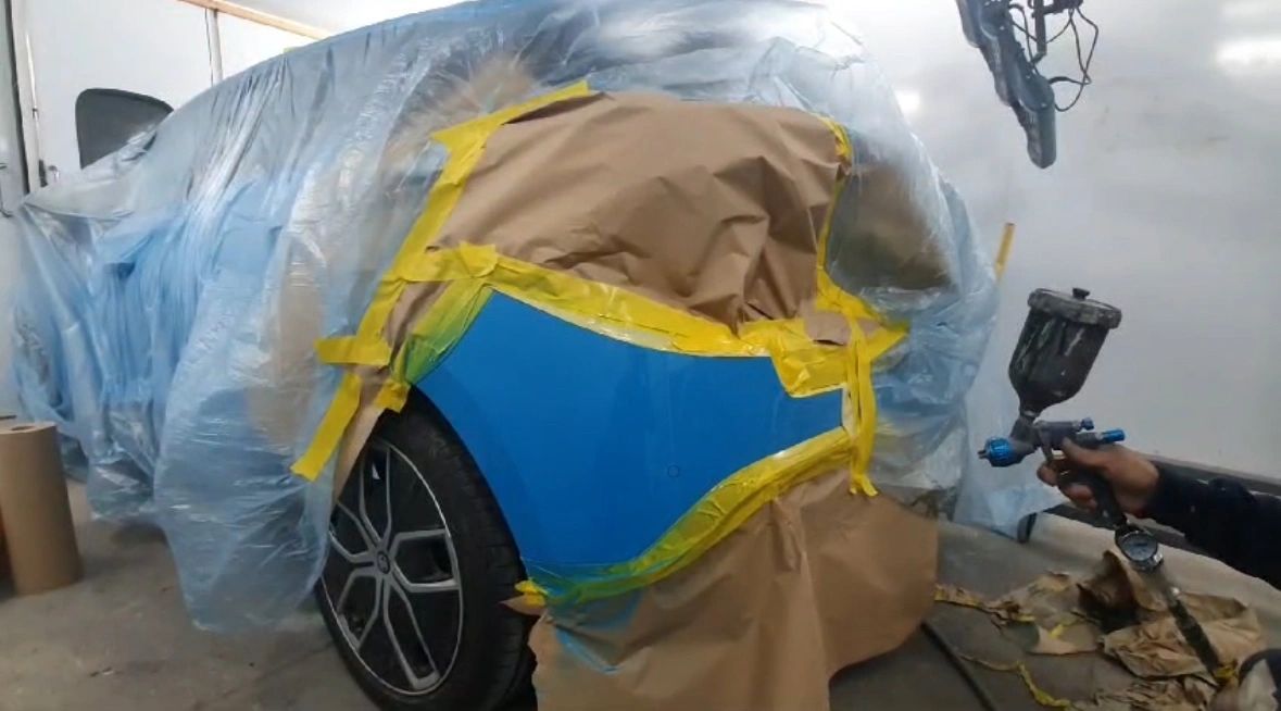 Blue paint being sprayed onto a rear quarter panel